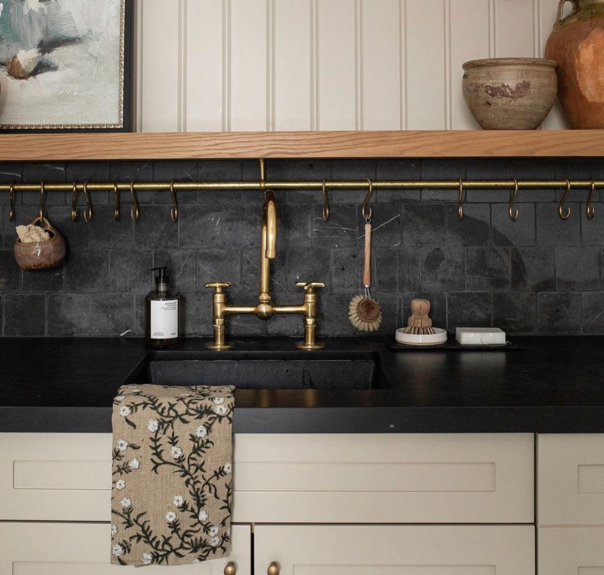 Tumbled black stone backsplash with a brass rail above a farmhouse sink