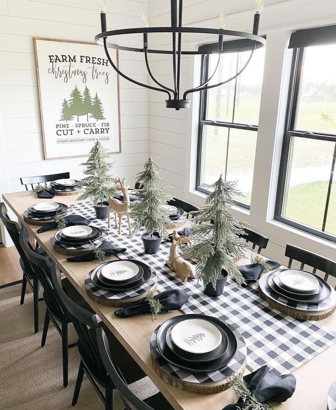 Buffalo-check runner with mini potted trees, black plates on wood chargers, and black chairs by bright windows.