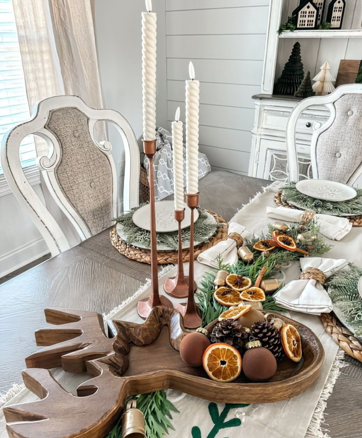 Rustic centerpiece with pinecones, dried oranges, evergreens, and twisty candles in a carved bowl.
