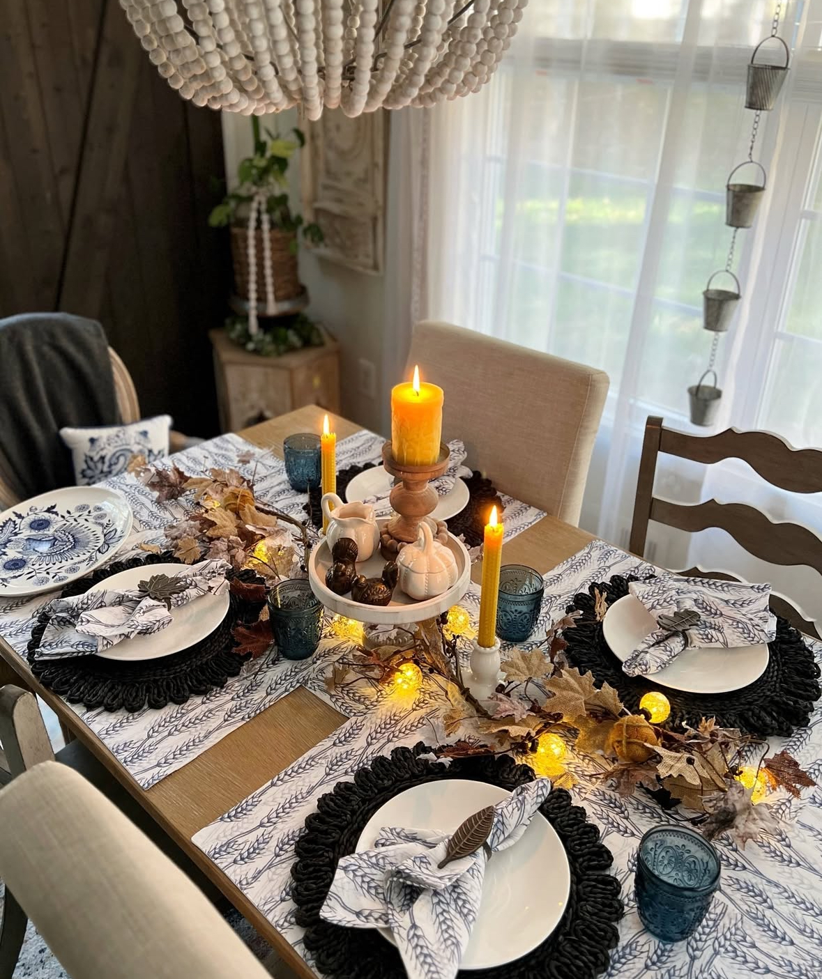 Moody fall dining table with mustard taper candles, twinkle lights, and dark chargers.
