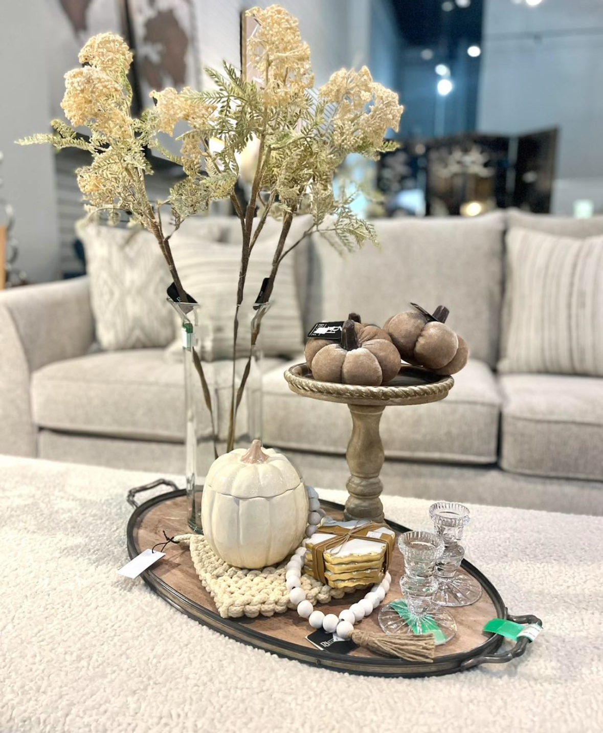 Neutral sofa with boucle ottoman; elongated tray styled with glass bud vases, pedestal of velvet pumpkins, beaded garland, and crystal candleholders.