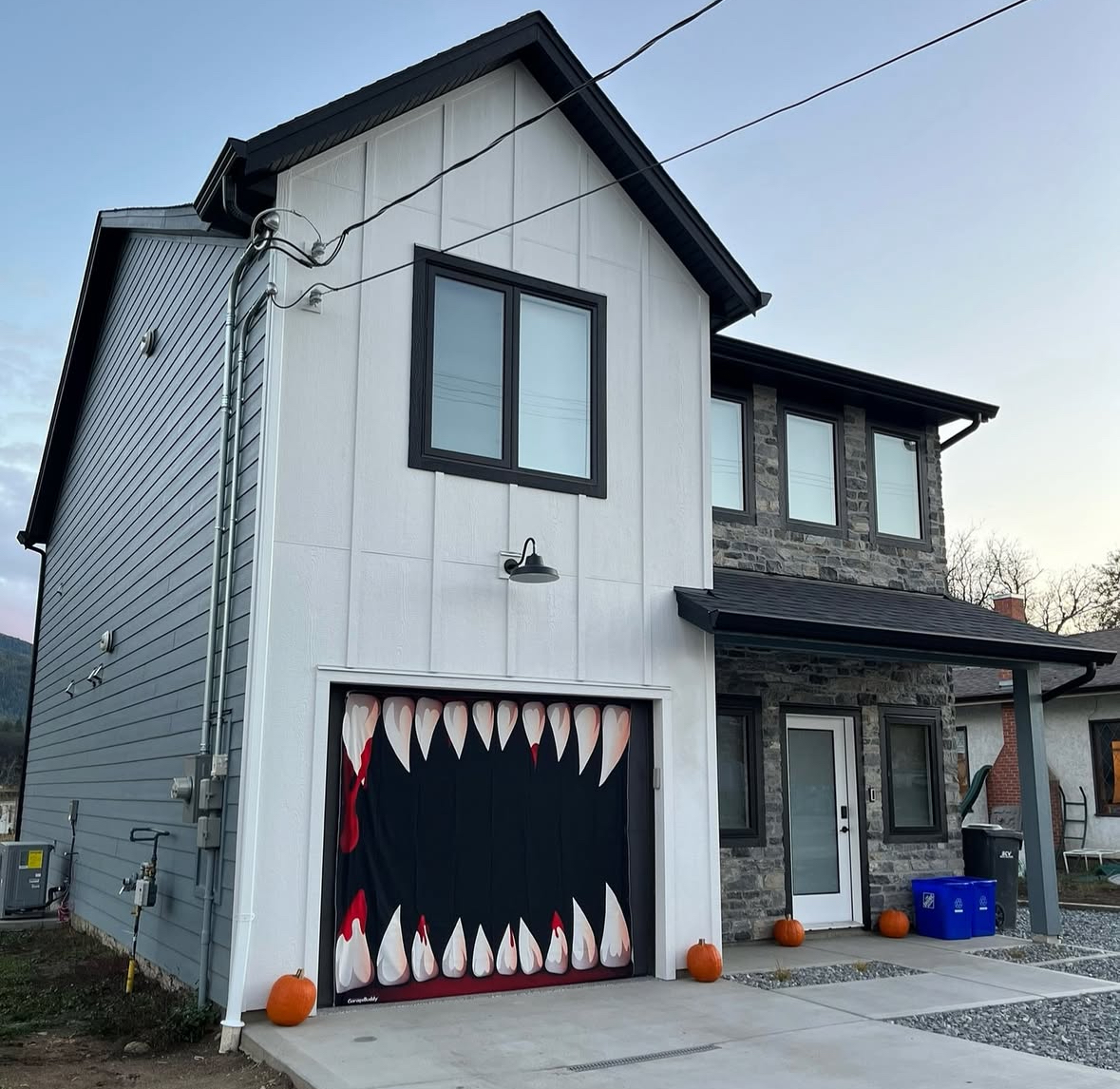 Garage door wrapped in a giant black-and-red monster mouth with rows of sharp, bloody teeth; small pumpkins placed along the driveway.