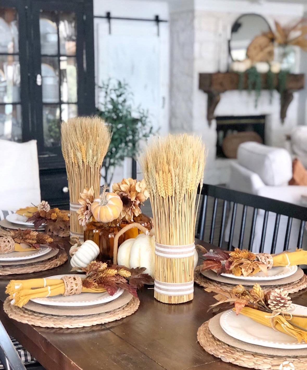 Harvest-inspired table with wheat bundles, stacked pumpkins, woven chargers, and amber glass.