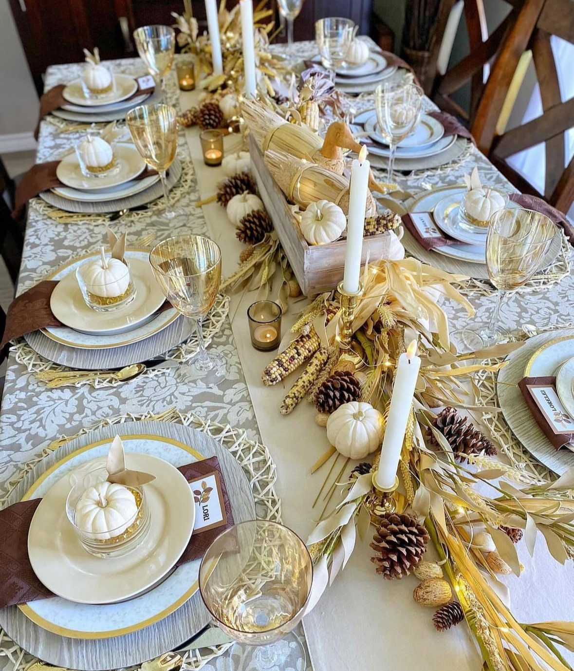 Neutral fall centerpiece of dried corn, pinecones, and ivory pumpkins along a simple runner.