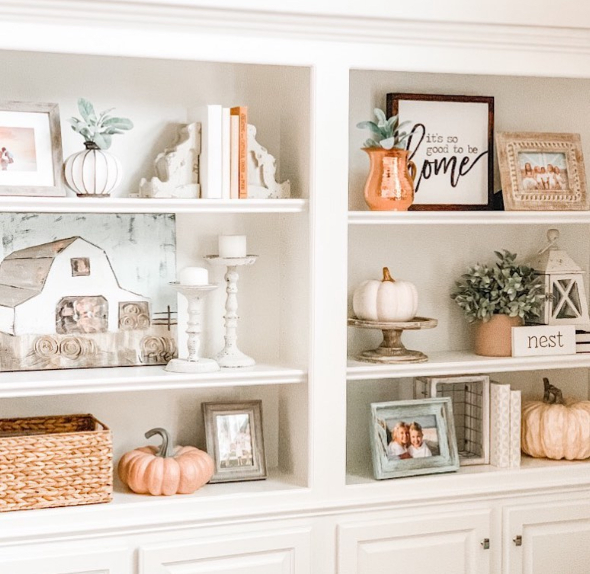 White built-ins styled with pumpkins, candles, greenery, lantern, and family photos in a light palette.
