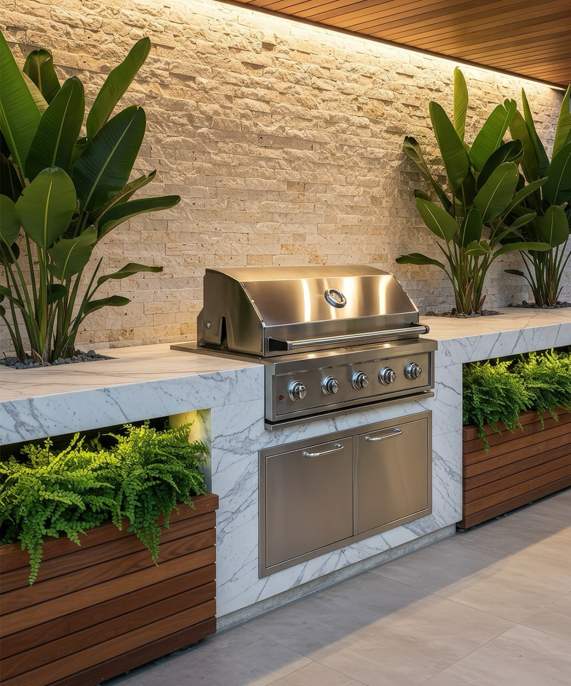 Marble-clad counter with stainless grill and lush planters against a lit stone wall offering resort-style outdoor kitchen ideas