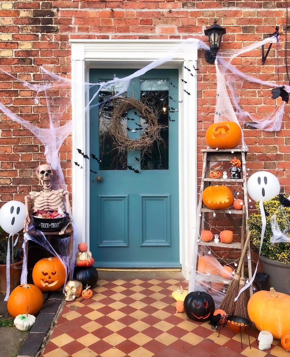 Blue door with spider webs, bats, skeleton candy butler, ladder stacked with jack-o’-lanterns, and ghost balloons.
