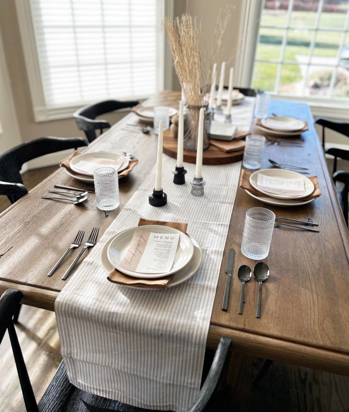 Minimal fall table with a striped runner, wheat stems, black flatware, and printed menus.