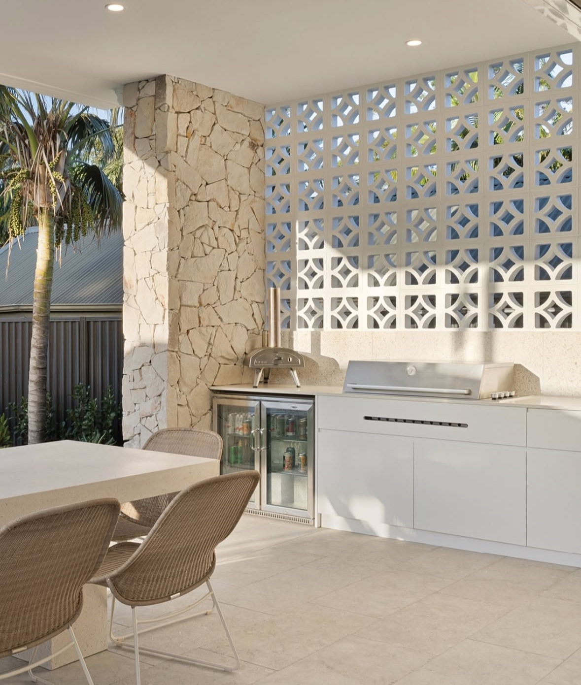 Covered lanai with geometric breeze-block screen, white cabinetry, and small pizza oven inspiring airy backyard outdoor kitchen ideas