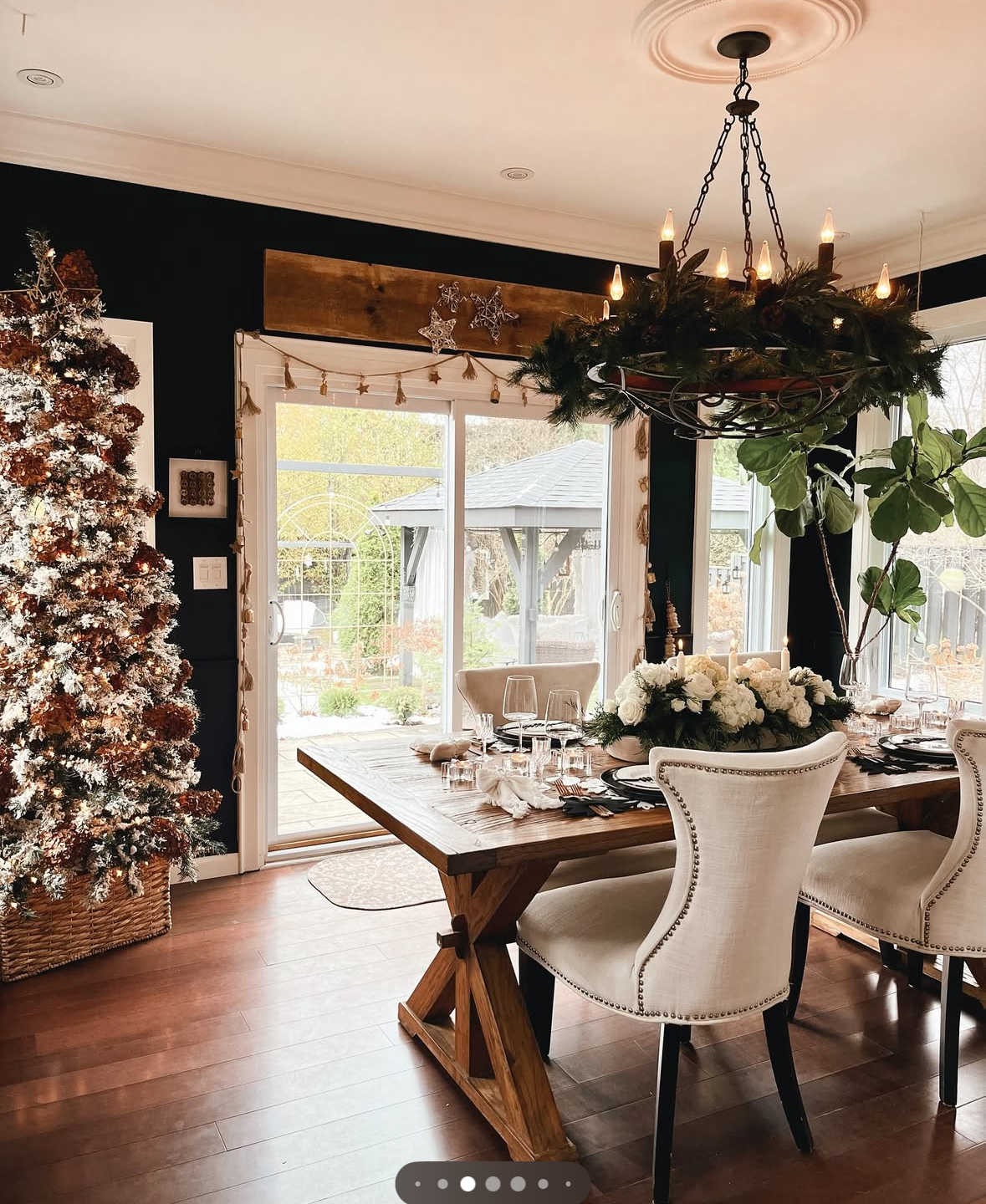 Black-walled room with frosted tree and white florals offering Christmas decoration ideas for dining room.