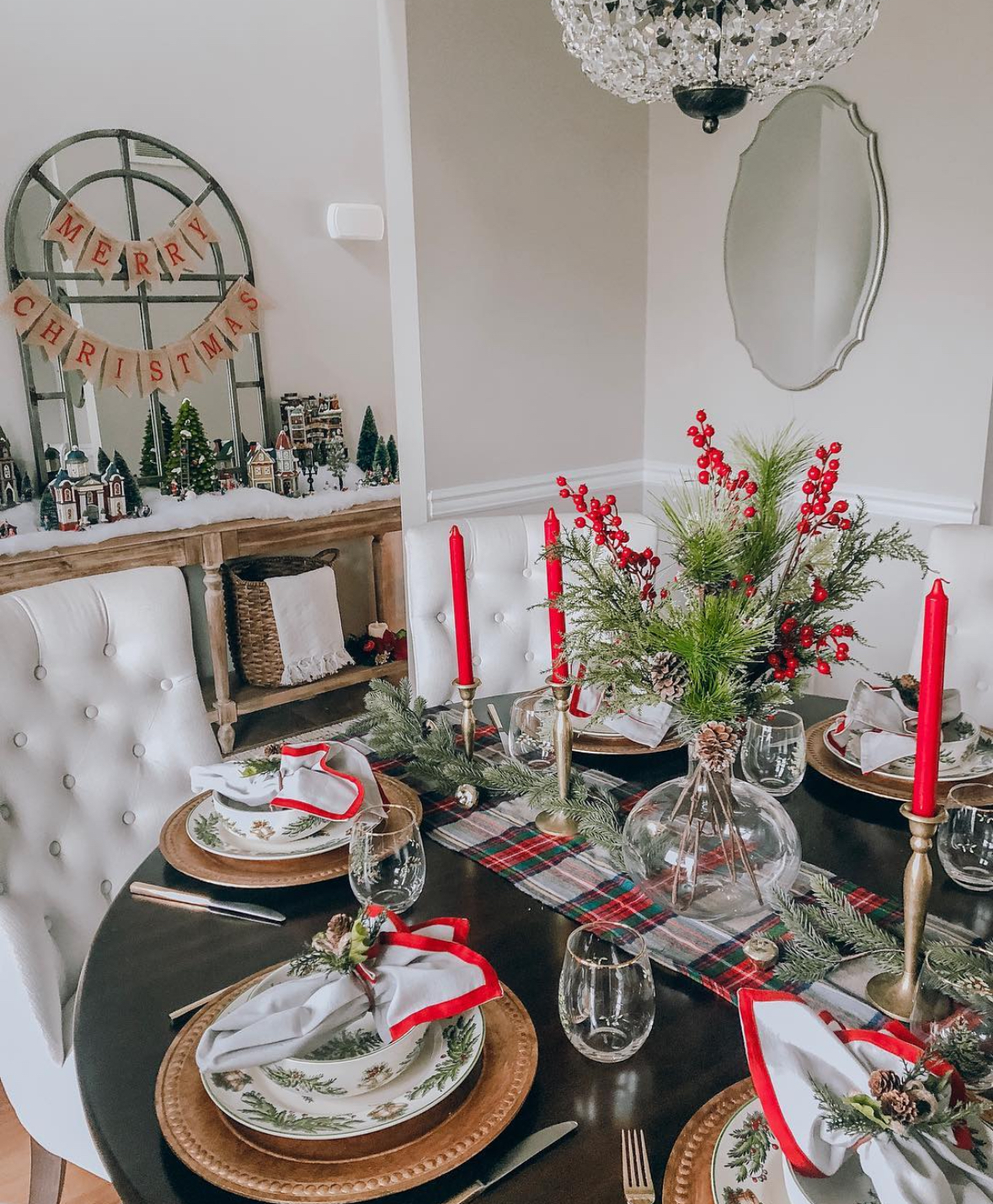 Round dining table with plaid runner, red taper candles, evergreen garland, and berry-filled centerpiece set for four.