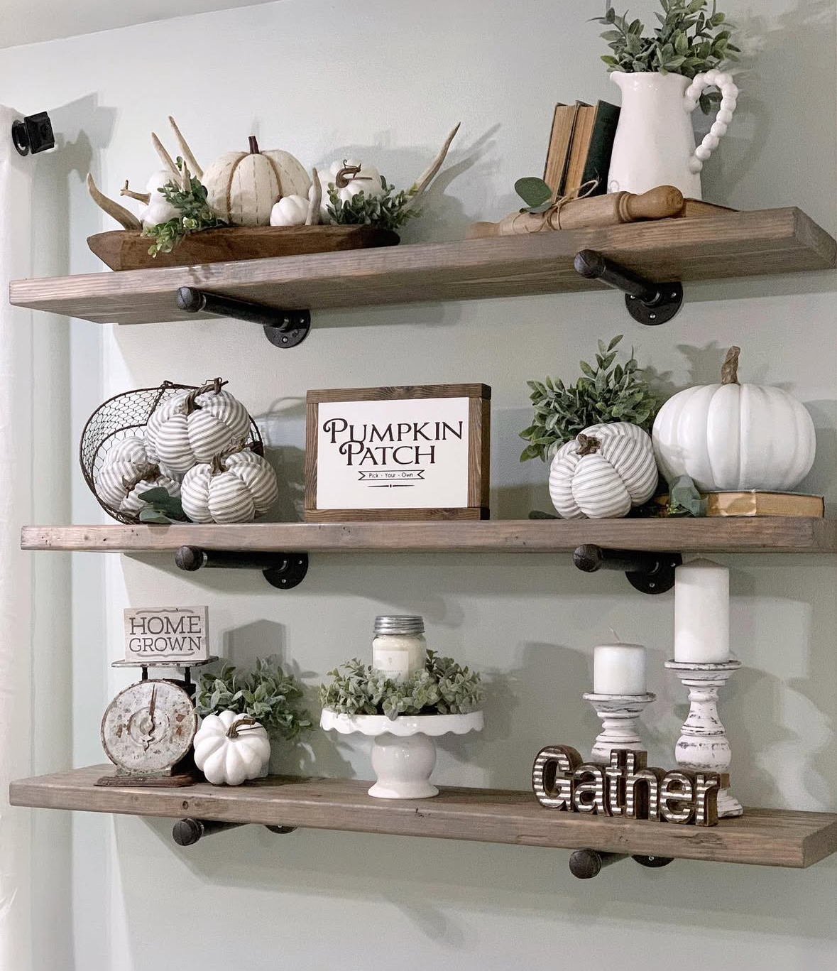 Three rustic pipe-supported shelves with “Pumpkin Patch” sign, striped pumpkins, candlesticks, and greenery.