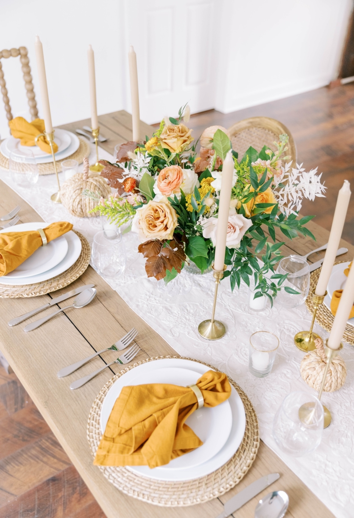 Bright fall table with woven chargers, brass tapers, garden florals, and mustard napkins.
